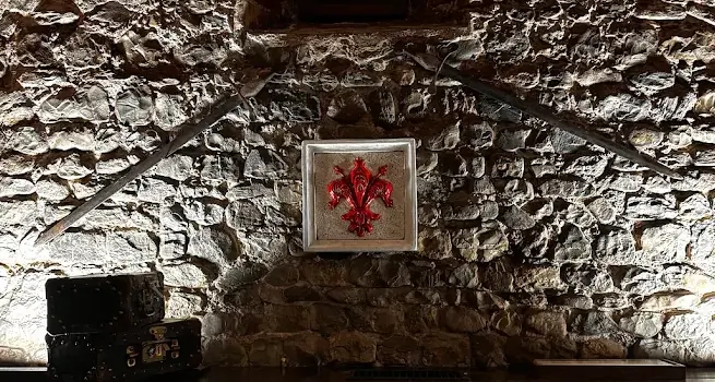 Dettaglio del muro di pietra: il giglio rosso di Firenze incorniciato, due spade incrociate e due vecchie valigie sulla credenza.
