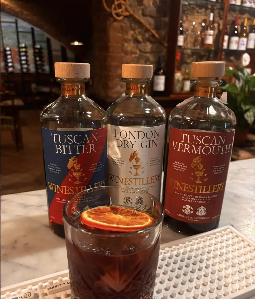 Un Negroni con fetta d'arancia disidratata sul bancone di marmo, davanti alle bottiglie di bitter, gin e vermouth toscani.