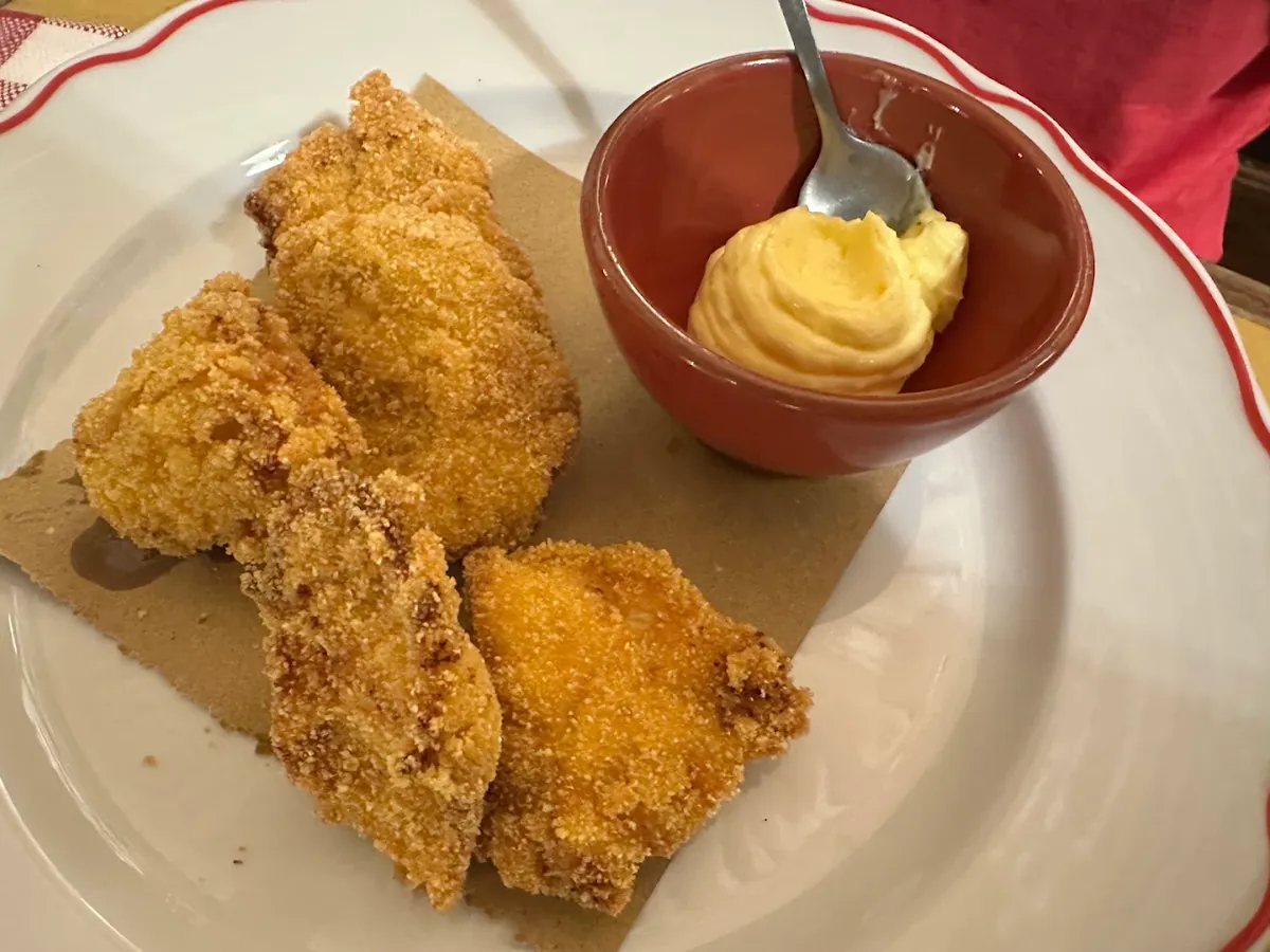 Pezzi di pollo fritto dorato su carta paglia, con una ciotolina di terracotta piena di maionese al limone.